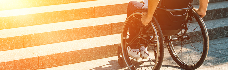 cropped image of a man using wheelchair on street and stopping near stairs without ramp